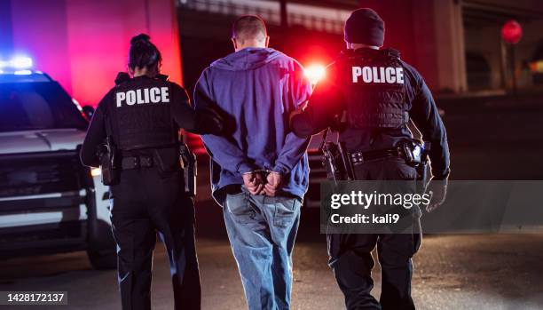 sospechoso esposado siendo arrestado por la policía por la noche - police officer fotografías e imágenes de stock