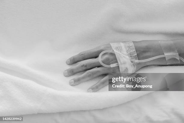 unidentified patient woman hand with receiving intravenous fluid directly into a vein while her resting on hospital bed. black and white tone. - boy lying dead stockfoto's en -beelden