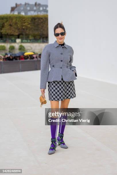 Gala Gonzalez wears grey pepita tailored blazer, checkered black white skirt, purple knee socks, heels, brown micro bag outside Dior during Paris...