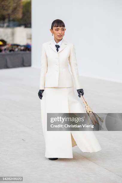 Guest wears beige bag, white wrapped skirt, black platform shoes, blazer, ties outside Dior during Paris Fashion Week - Womenswear Spring/Summer 2023...