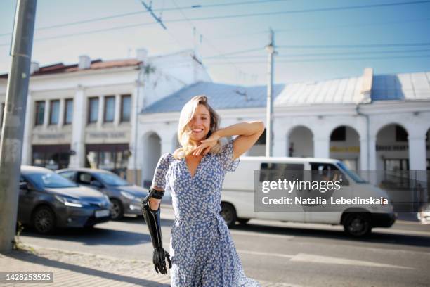 young woman blonde with prosthetic arm dances on street of city. - artificial arm stock pictures, royalty-free photos & images