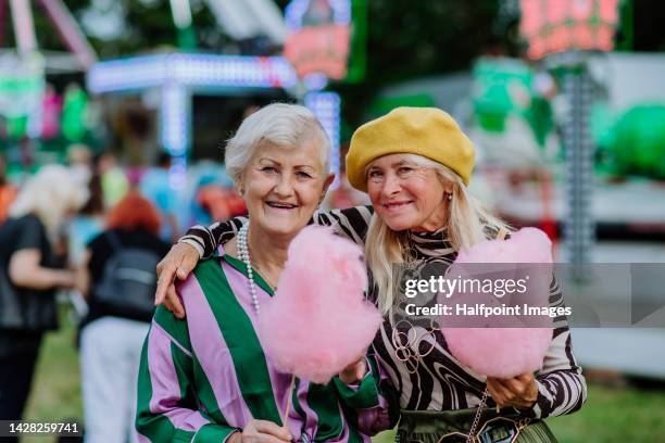 happy senior friends enjoying county fair, eating cotton candy. - carousel musical fotografías e imágenes de stock