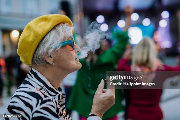 portrait of happy senior woman smoking and enjoying city night life. - smoking cigarette stock-fotos und bilder