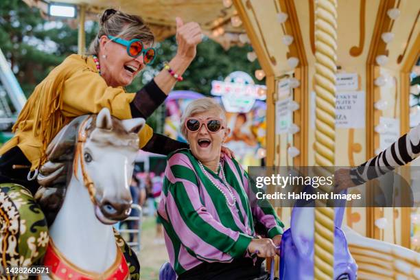happy senior friends enjoying county fair at carousel. - carrossel imagens e fotografias de stock