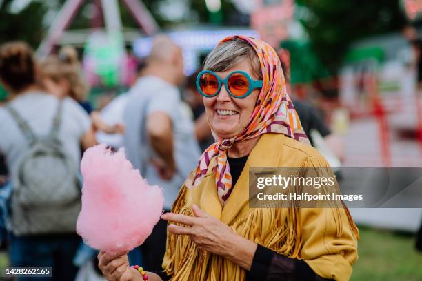 cheerful senior woman enjoying county fair, eating cotton candy. - young at heart stock pictures, royalty-free photos & images