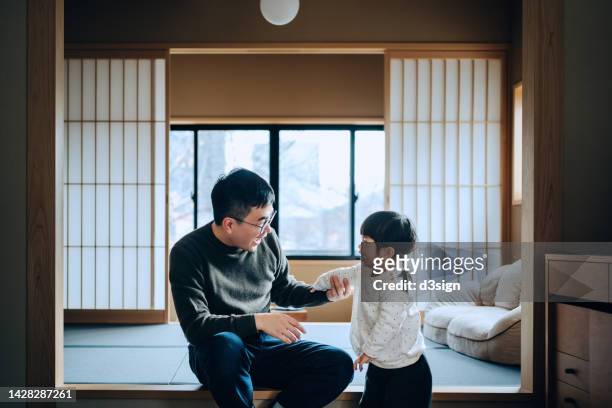 loving young asian father with her cute little daughter sitting on tatami mat in a traditional japanese style wooden apartment, chatting and enjoying father and daughter bonding time. family lifestyle. love and care concept - ryokan foto e immagini stock