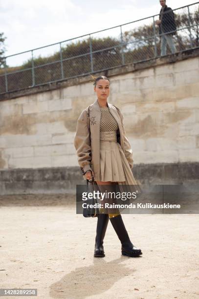 Sarah Lysander wearing a beige pleated mini skirt, beige jacket with embroidered flowers, long black boots, and black Dior bag outside Christian...
