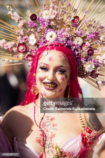 Guest wearing a pink dress, a golden crown with pink and white flowers, bright pink hair, full glam makeup, and body painting outside Christian Dior,...