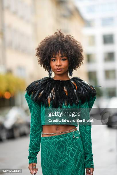 Sarah Monteil wears silver large earrings, a green embroidered print pattern with embroidered black feathers collar, a matching green embroidered...