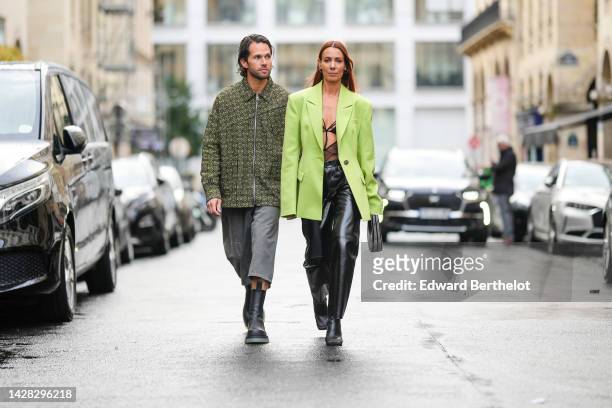 Rocques wears a black with green logo print pattern oversized zipper jacket from Loewe, gray ripped denim short pants, black shiny leather ankle...