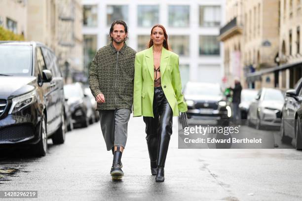 Rocques wears a black with green logo print pattern oversized zipper jacket from Loewe, gray ripped denim short pants, black shiny leather ankle...