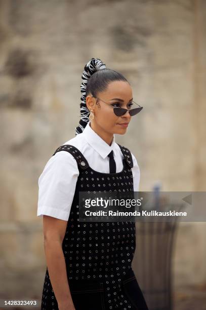 Sai De Silva wearing white shirt, black tie, black dress with crystals, black Dior socks, and Dior shoes and hair in a pony tail decorated with metal...