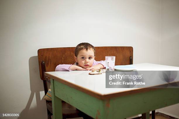 a young kid sits at a table with here food - hunger stock-fotos und bilder