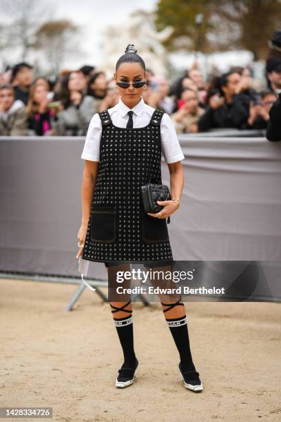 Sai De Silva wears black cat eyes sunglasses, a silver leather laces ponytail, a white short sleeves shirt from Dior, a black tie from Dior, a black...