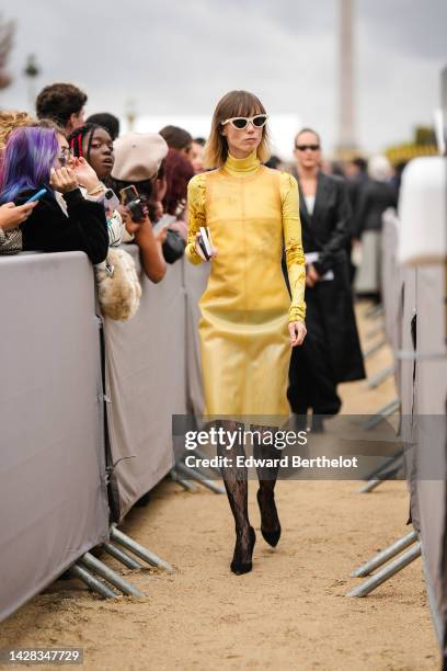 Anya Ziourova wears beige cat eyes sunglasses, a yellow with brown flower pattern turtleneck / long sleeves pullover from Dior, a yellow sleeveless /...