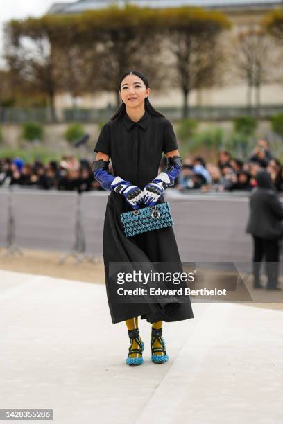 Yuwei Zhangzou wears a black short sleeves / long pleated dress from Dior, a black / blue / white shiny leather high biker gloves from Dior, a black...