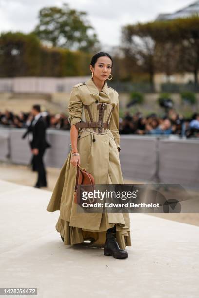 Yoyo Cao wears gold earrings, a beige long trench coat from Dior, a beige and brown laces corset, diamonds bracelets, a brown camel shiny leather...