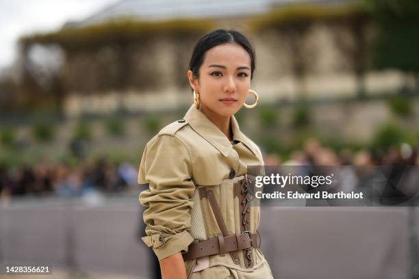 Yoyo Cao wears gold earrings, a beige long trench coat from Dior, a beige and brown laces corset, outside Dior, during Paris Fashion Week -...