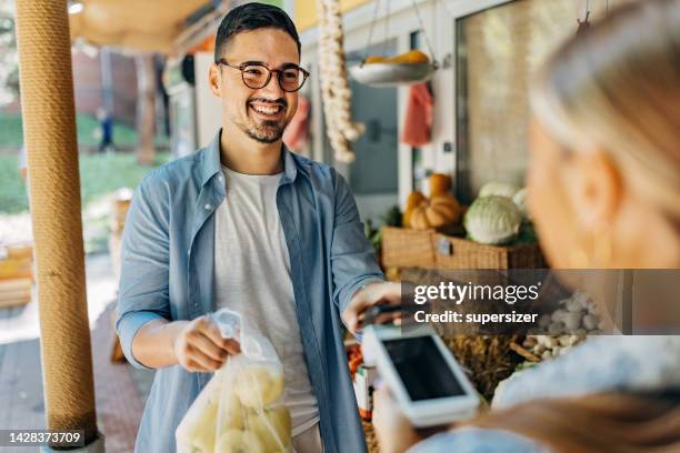 ein lächelnder mann bezahlt die rechnung telefonisch - straßenverkäufer stock-fotos und bilder