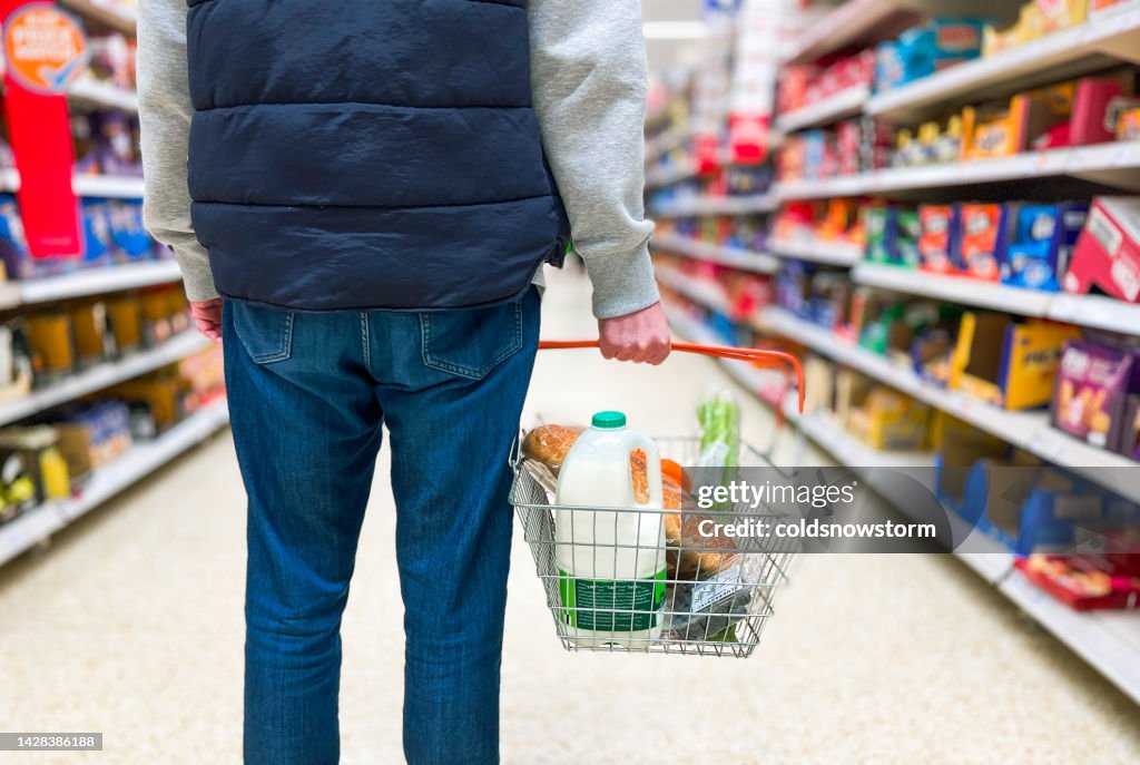Hombre sosteniendo canasta de compras con pan y comestibles de leche en el supermercado