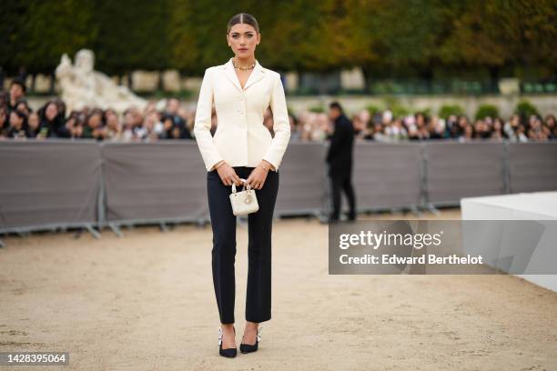 Amelie Zilber wears a gold with embroidered diamonds necklace, a white latte blazer jacket, black suit pants, a gold bracelet, a white pearls micro...