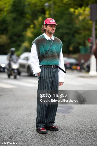 Rocques wears a red with embroidered white Marlboro pattern denim cap, a white shirt, a black and green gradient print pattern sleeveless wool...