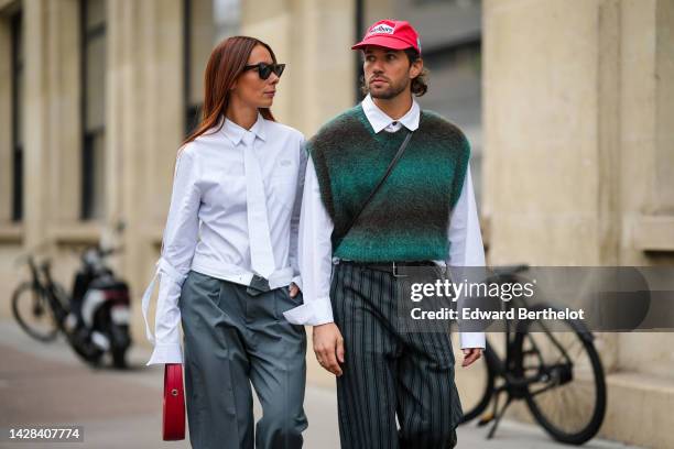 Alice Barbier wears black sunglasses, a white shirt, a white tie, dark gray large suit pants, a red shiny leather handbag from Coperni, ; JS Rocques...