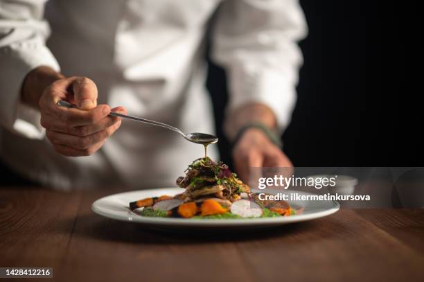 ein männlicher koch, der sauce auf die mahlzeit gießt - gourmet stock-fotos und bilder