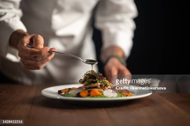 un chef masculin versant de la sauce sur le repas - aliment photos et images de collection
