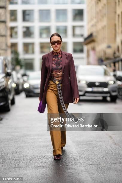 Guest wears brown sunglasses, gold earrings, a brown and black tiger print pattern high neck t-shirt, a burgundy blazer jacket, a black shiny leather...