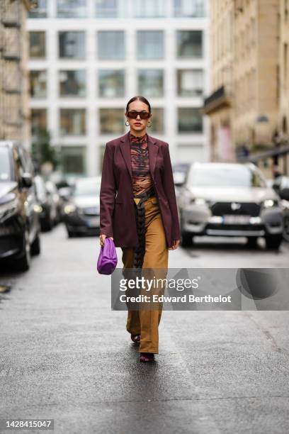 Guest wears brown sunglasses, gold earrings, a brown and black tiger print pattern high neck t-shirt, a burgundy blazer jacket, a black shiny leather...