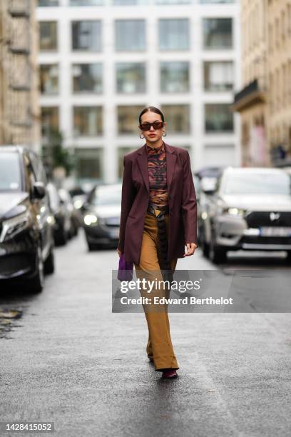 Guest wears brown sunglasses, gold earrings, a brown and black tiger print pattern high neck t-shirt, a burgundy blazer jacket, a black shiny leather...