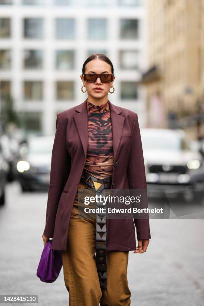 Guest wears brown sunglasses, gold earrings, a brown and black tiger print pattern high neck t-shirt, a burgundy blazer jacket, a black shiny leather...