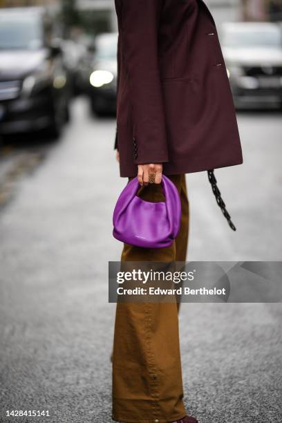 Guest wears a burgundy blazer jacket, a black shiny leather braided belt, a purple shiny leather handbag, brown large pants, outside Koche, during...