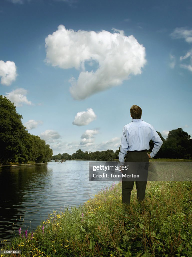 Businessman examining question mark in clouds