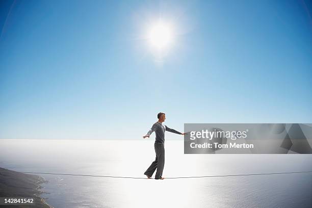 man walking tightrope over still ocean - cable photos et images de collection