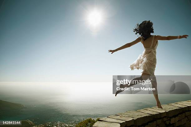 woman walking on stone wall on cliff - jumping sun stock pictures, royalty-free photos & images