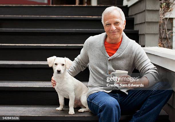 older man petting puppy on steps outdoors - middle age man with dog stockfoto's en -beelden