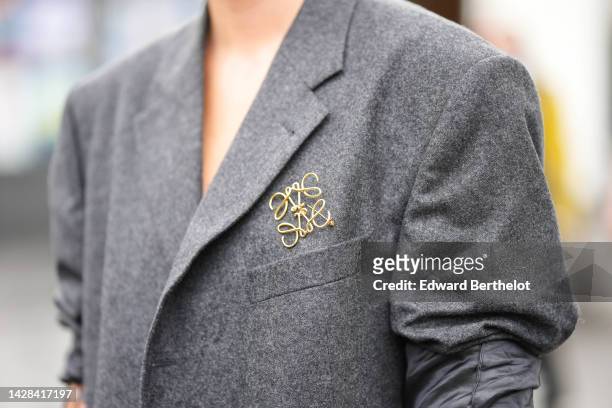 Guest wears a dark gray oversized blazer jacket, gold and silver rings, a gold logo brooch from Loewe, outside Koche, during Paris Fashion Week -...