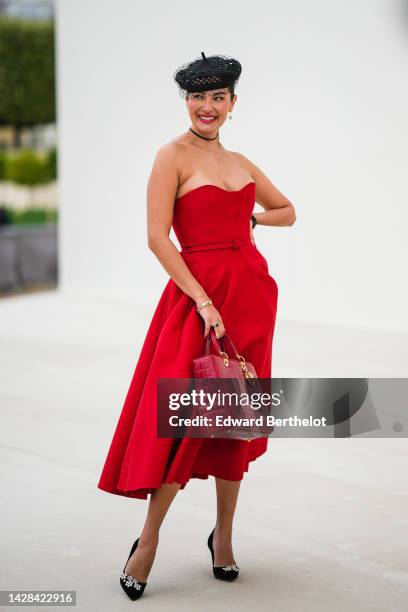 Guest wears a black cut-out with embroidered mesh / fishnet yoke beret hat from Dior, a black necklace from Dior, a gold chain necklace, a red...