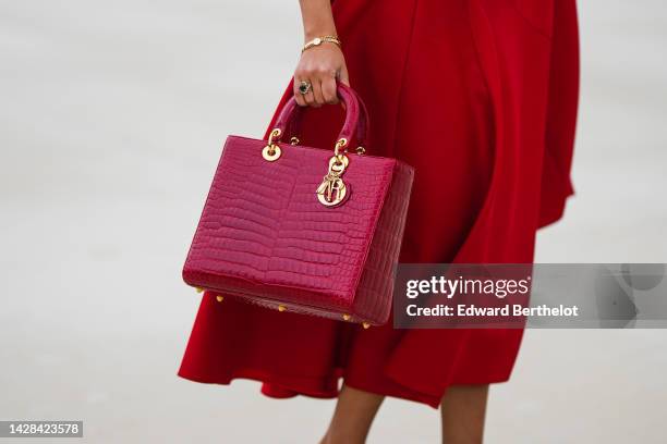 Guest wears a red shoulder-off midi dress from Dior, a red shiny leather crocodile print pattern large Lady D-Light handbag from Dior, gold...