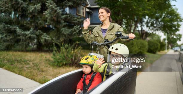 smiling mom and her sons waving at neighbors from a cargo bike - zwaaien gebaren stockfoto's en -beelden