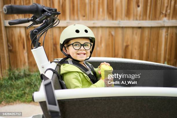 smiling boy drinking juice in the cart of his parent's cargo bike - sports helmet stock pictures, royalty-free photos & images