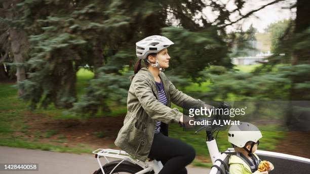 smiling mom riding a cargo bike in a park with her little boy - ebike stockfoto's en -beelden