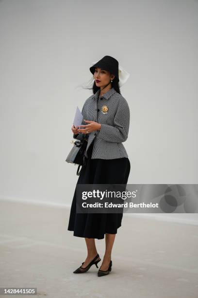 Guest wears a black felt bob hat, a black midi dress, a black and white checkered print pattern belted jacket from Dior, a gold and white pearls eyes...