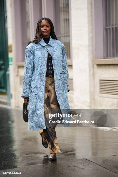 Guest wears a black turtleneck / silver buttoned pullover, a pale blue denim with navy blue embroidered flower pattern long coat, a black shiny...