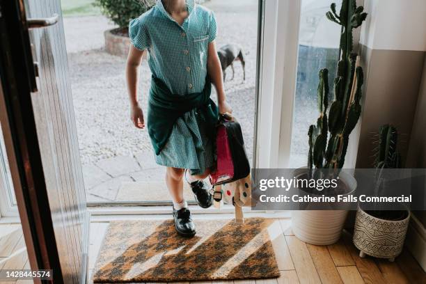 a child enters through a domestic doorway after school, wearing a school uniform dress. - school uniform uk stock pictures, royalty-free photos & images