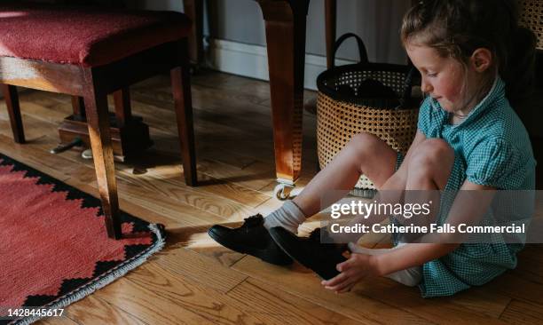 a little girl pulls on a pair of patented school shoes before leaving for school. she pulls on a pair of black, patent school shoes. - girls in socks stockfoto's en -beelden