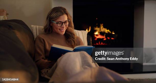 femme dans la cheminée du salon lisant un livre de comédie pour les loisirs ou les divertissements intérieurs d’hiver ou de nuit. lecteur de rat de bibliothèque avec des lunettes profitant d’une histoire de fiction littéraire à l’intérieur d� - foyer de cheminée photos et images de collection