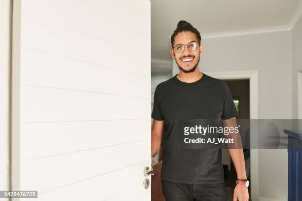 young man opening the front door and smiling - front door open stock pictures, royalty-free photos & images